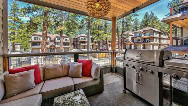Un espacio exterior moderno para disfrutar al aire libre, con un sofá, una parrilla y grandes ventanales con vistas a un barrio residencial.