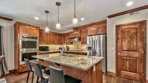 Una cocina con armarios de madera, electrodomésticos de acero inoxidable, encimera de granito e iluminación colgante.
