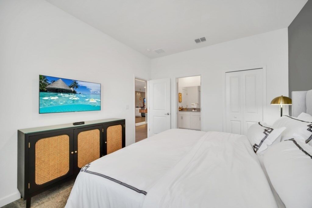 Ein Hotelzimmer mit einem großen Bett, einem an der Wand befestigten Fernseher, einem Korbmöbel und einer Tür zu einem Badezimmer.