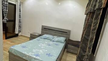 A bedroom with a wooden ceiling, a bed with a floral bedspread, a nightstand, and a window with curtains.
