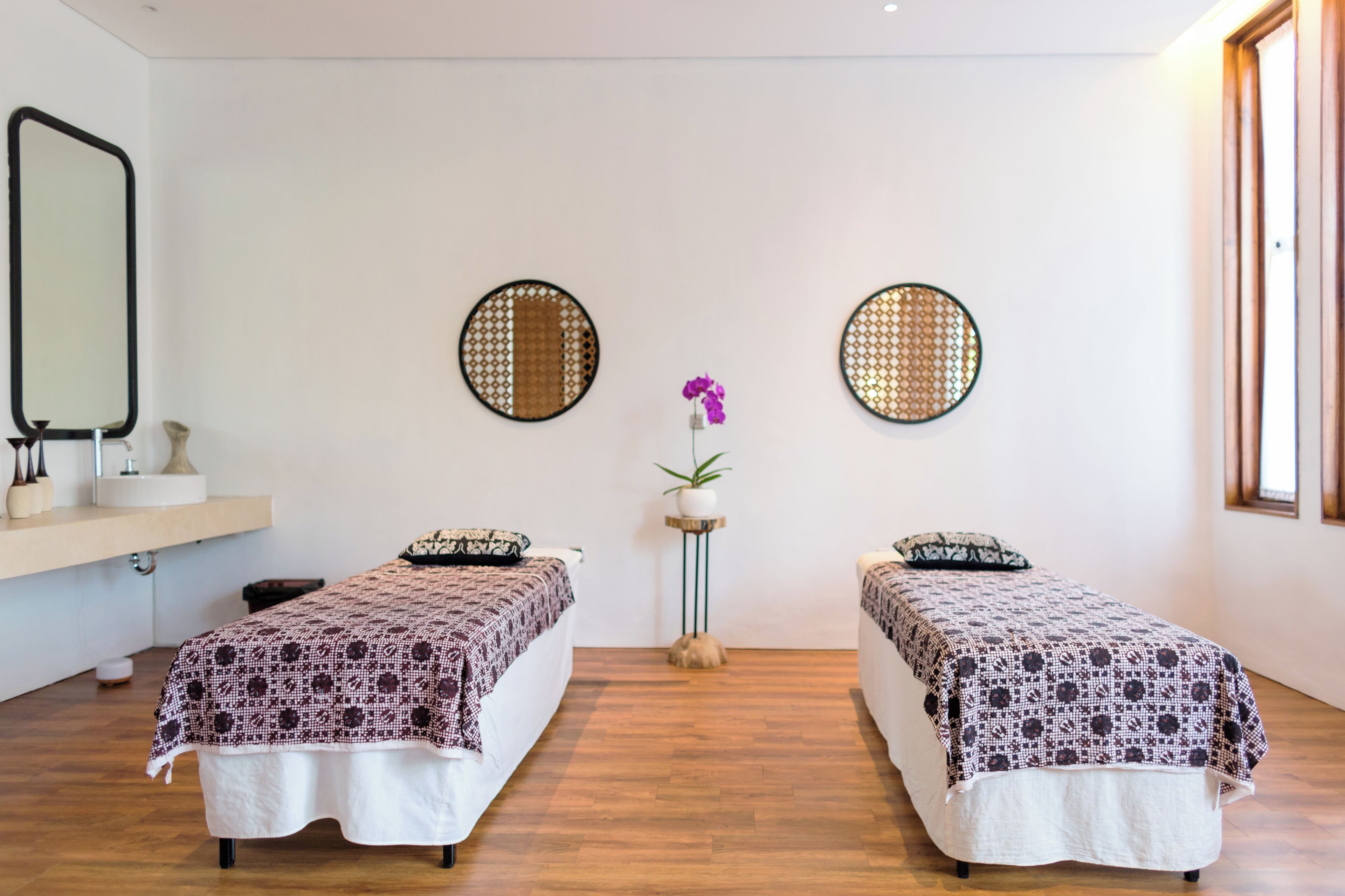A room with two beds, a mirror, and two round mirrors on the wall.