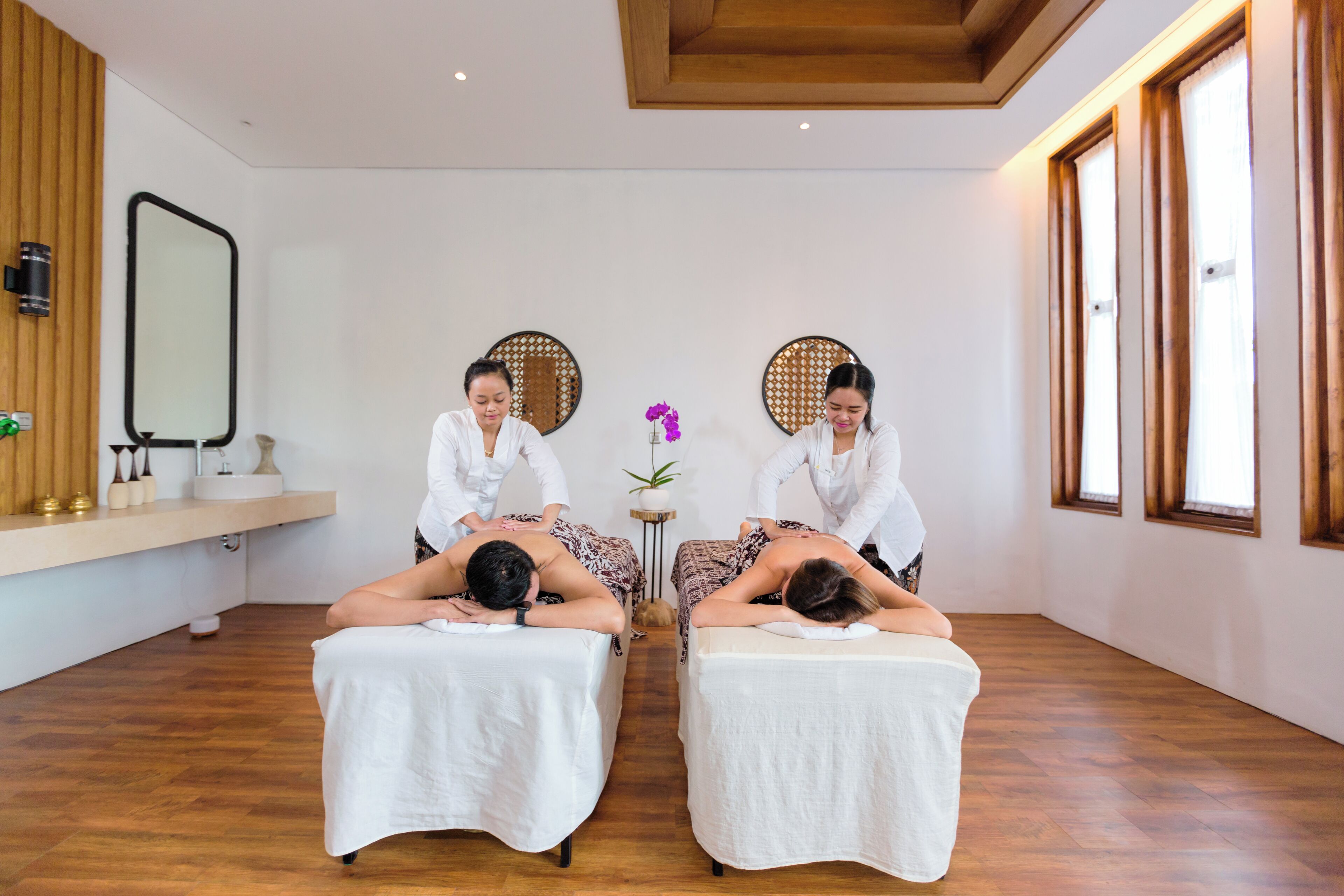 Une salle de spa équipée de deux tables de massage, dotée d’un plancher en bois et de grandes fenêtres.