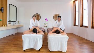 Une salle de spa équipée de deux tables de massage, dotée d’un plancher en bois et de grandes fenêtres.