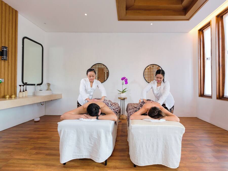 Une salle de spa équipée de deux tables de massage, dotée d’un plancher en bois et de grandes fenêtres.