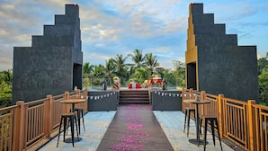 A covered outdoor area with a wooden deck, a pink flower aisle, and a stage with tables and chairs. - Hotel Le Temple (Borobudur)