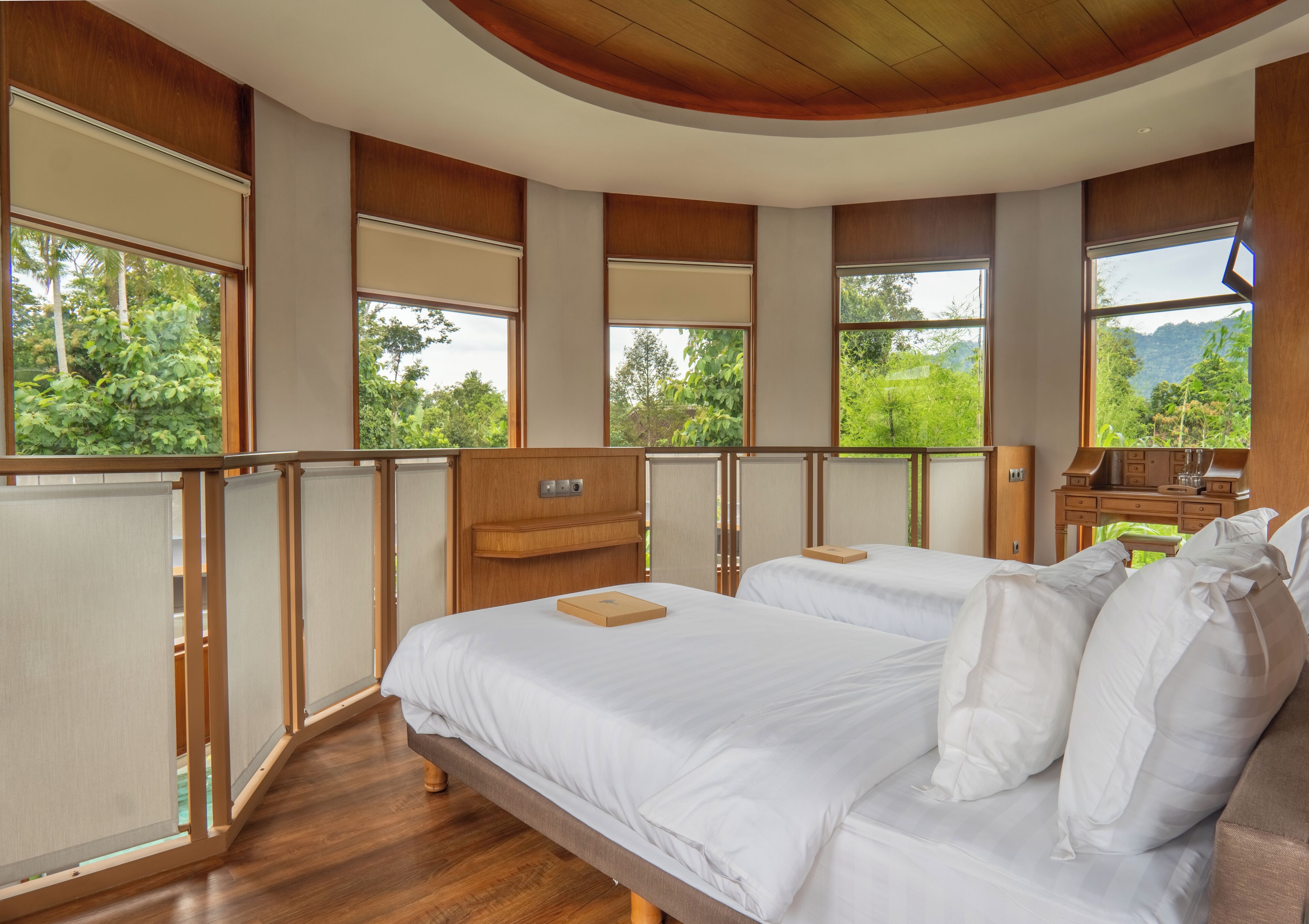 A bedroom with two beds, a wooden ceiling, and large windows offering a view of greenery.