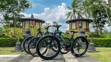 A bicycle rack with multiple bicycles parked in a garden area with stone statues and a gazebo in the background.