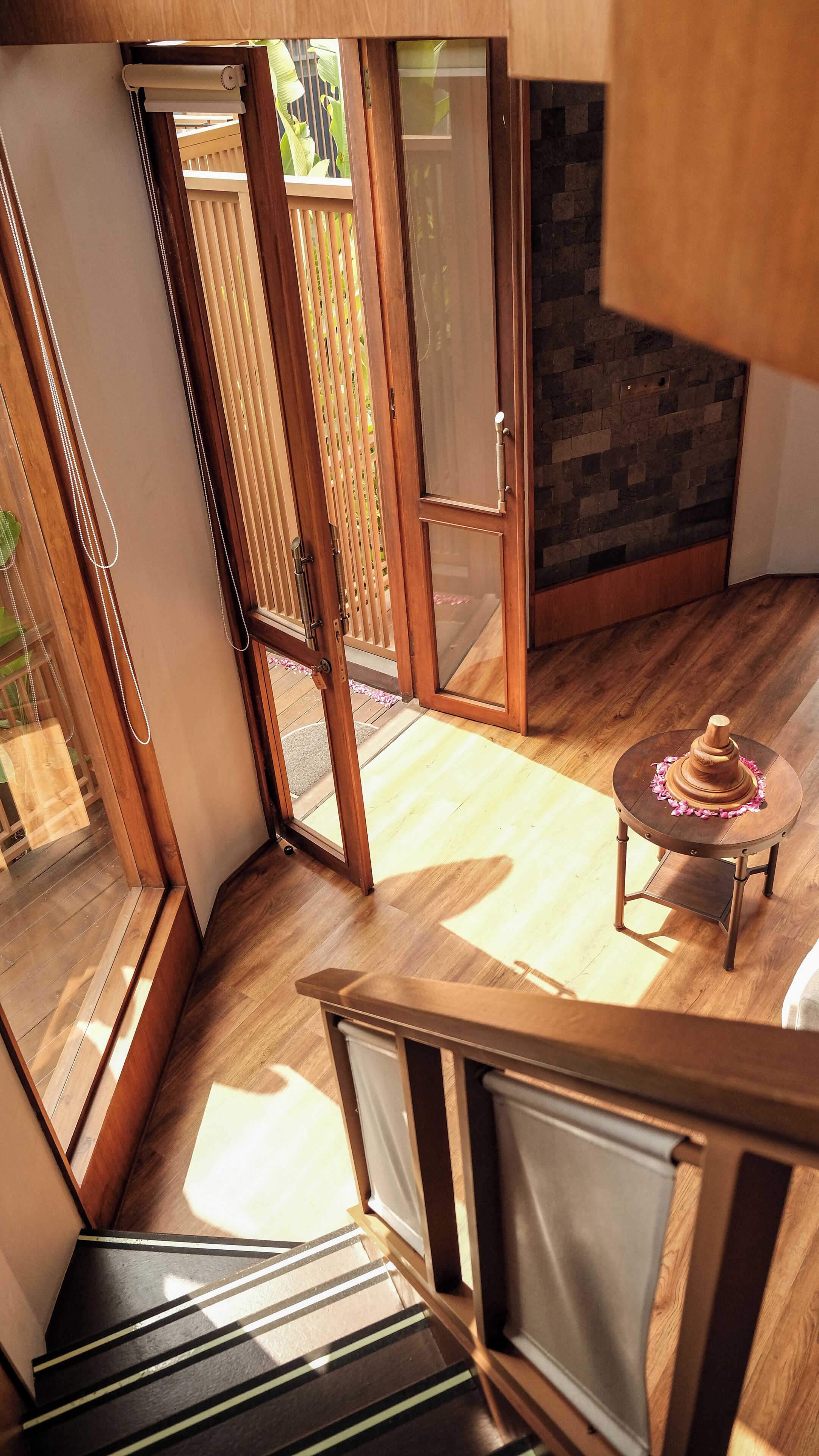 Ein modernes Interieur mit einer Holztreppe, einem kleinen runden Tisch und einem dekorativen Gegenstand, sowie Blick auf eine Holzterrasse.