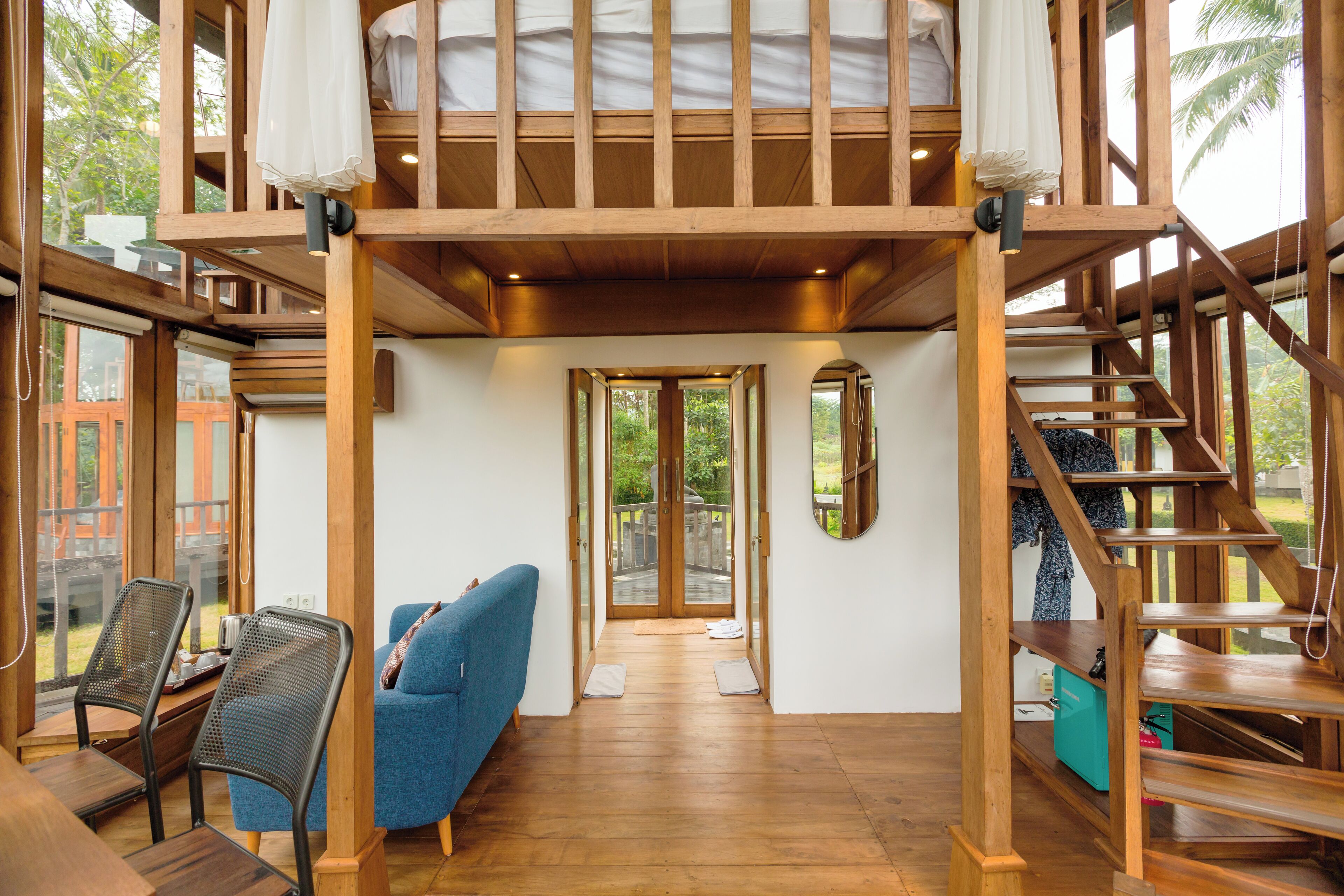 Una habitación amplia con piso de madera, un sofá azul y una escalera que conduce a un nivel superior.
