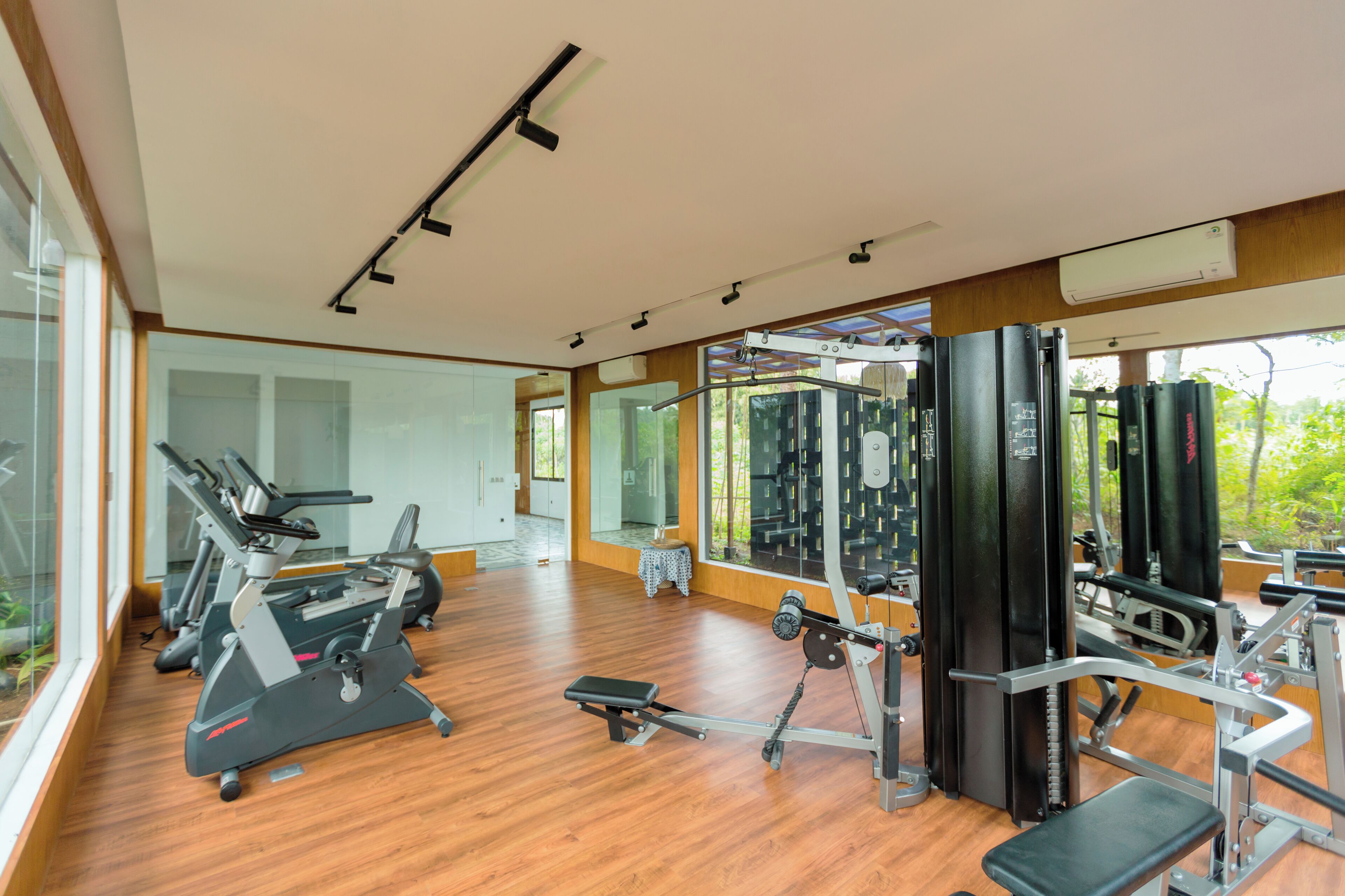 Un gimnasio con equipo de ejercicio, ventanas amplias y suelo de madera.
