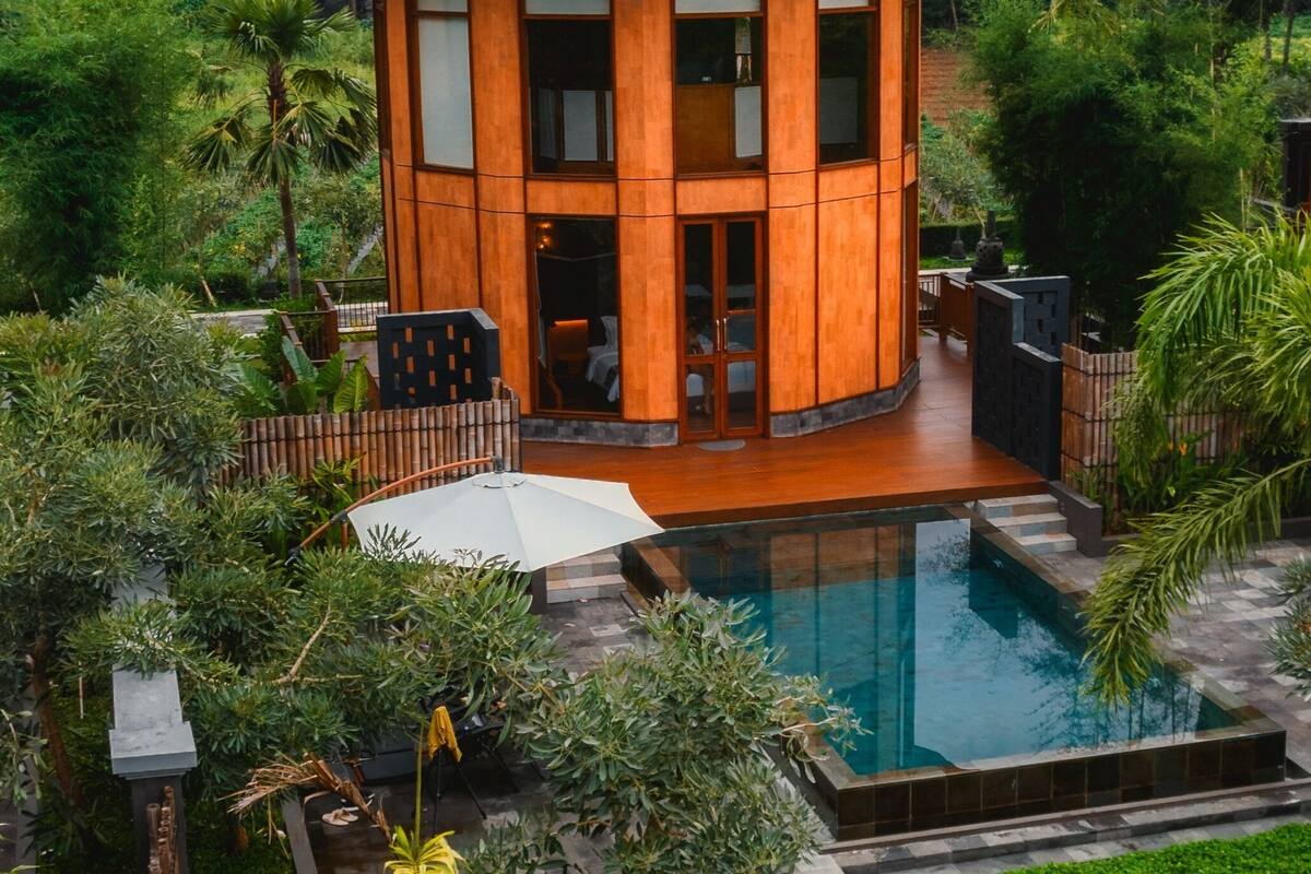 Una casa moderna con piscina, rodeada de exuberante vegetación y montañas al fondo.