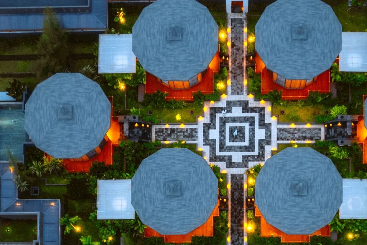 Distribución simétrica con cuatro estructuras octogonales conectadas por un sendero central, rodeadas de vegetación e iluminadas por luces cálidas.