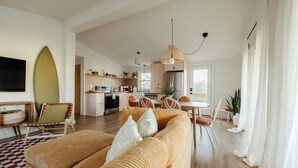 A modern living room with a sofa, dining area, kitchen, and a large window. - The Haven • Outdoor Tub • Backyard Oasis • As seen on Magnolia Network (Kill Devil Hills)