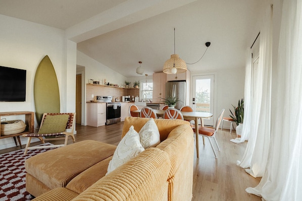 A modern living room with a sofa, dining area, kitchen, and a large window.