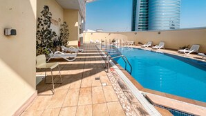 A rooftop pool area with sun loungers and a view of a modern building. - Cosmos Living Goldcrest Executive  (Dubai)