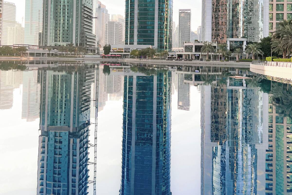 A modern high-rise building with a curved facade, surrounded by other tall buildings, reflecting in a calm body of water.