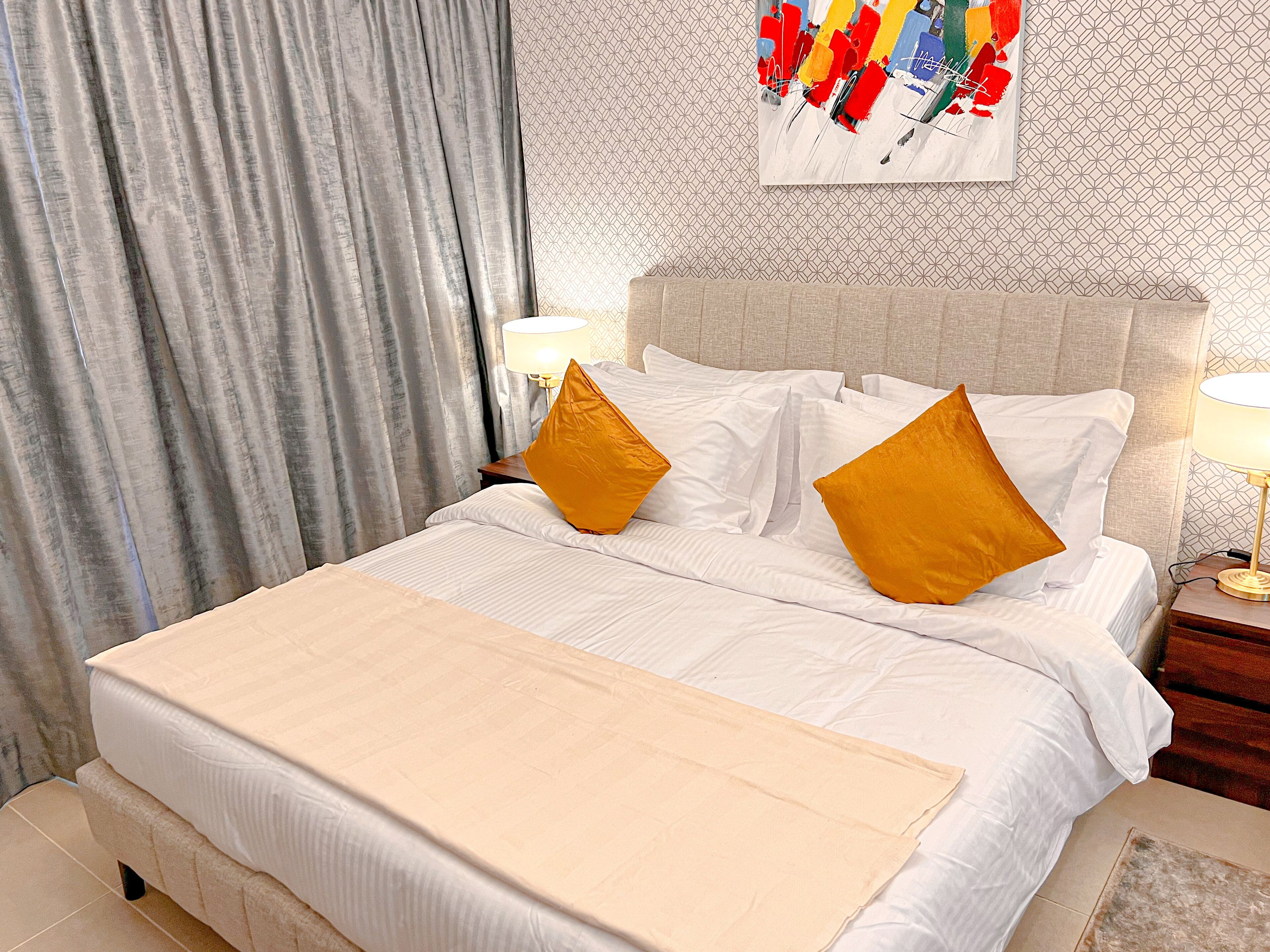 Una habitación de hotel con una cama bien tendida, una mesita de noche con lámpara y una pared con diseño geométrico.