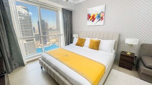A hotel room with a large bed, a view of a cityscape through a floor-to-ceiling window, a modern chandelier, and a painting on the wall. - Cosmos Living Goldcrest Executive  (Dubai)