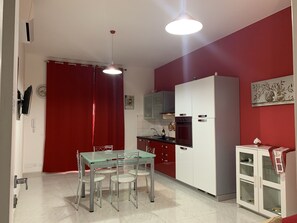 Cozinha compacta com armários brancos, mesa de jantar de vidro e detalhes vermelhos nas paredes.