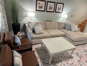 A living room with a sectional sofa, a coffee table, a potted plant, and a staircase. - Warm Coastal Retreat Near St Augustine (St. Augustine)