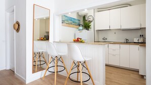 A modern kitchen with white cabinets, a wooden countertop, and two white bar stools with wooden legs. - Renovated apartment in Candelaria (CN)