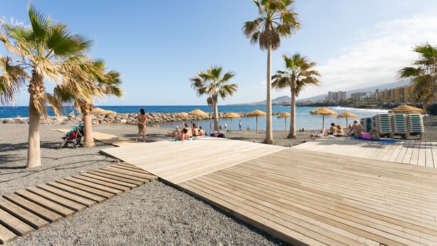 A beach with palm trees, a wooden deck, and umbrellas. - Renovated apartment in Candelaria (CN)