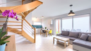 Un salon moderne avec un escalier, un coin repas et une cuisine en arrière-plan.
