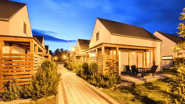 Une rangée de maisons modernes à un étage, séparées par un chemin pavé, chacune dotée d’un petit patio et d’un espace aménagé pour s’asseoir à l’extérieur.