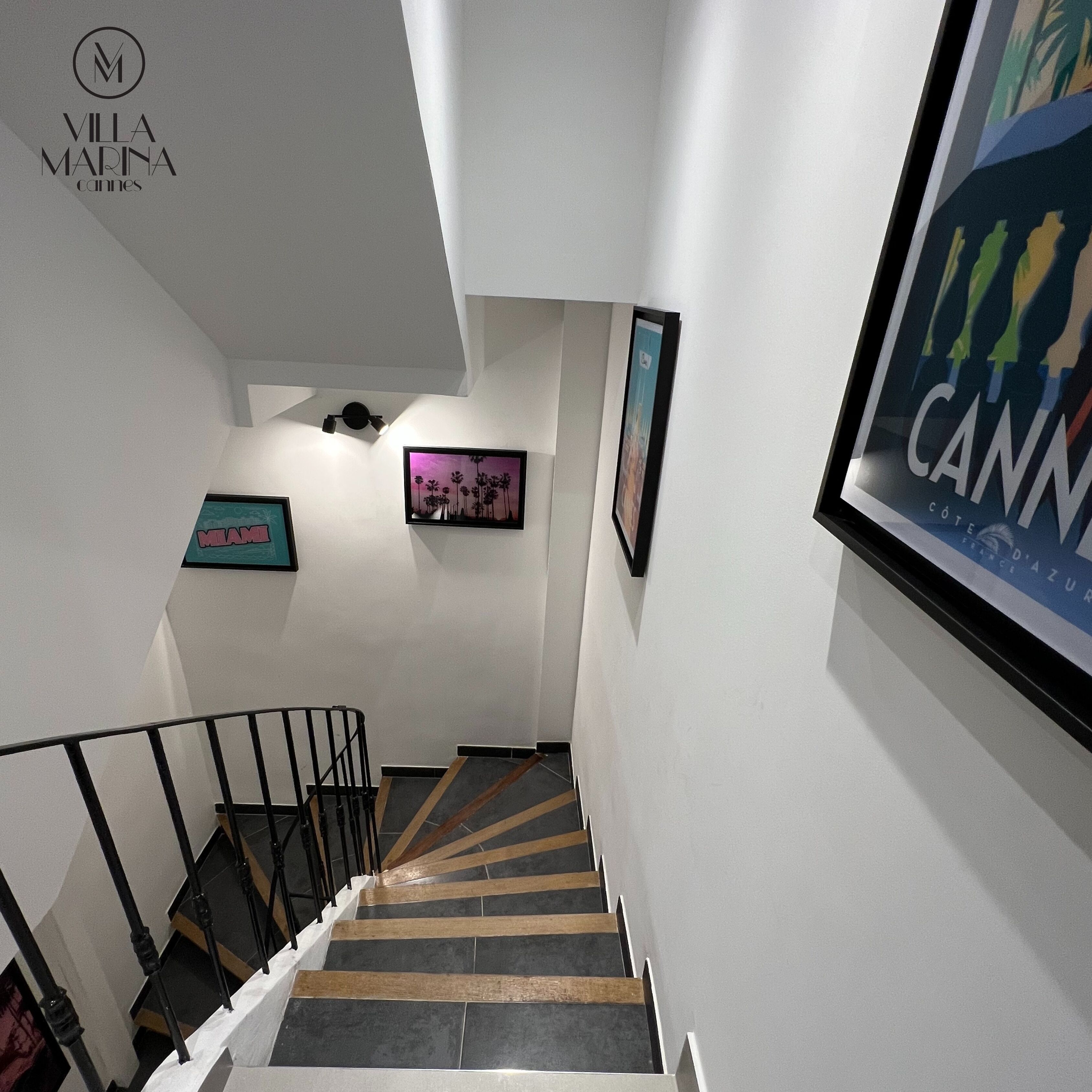 A staircase with a handrail, leading to a landing with framed artwork and a sign reading "VILLA MARINA Cannes".