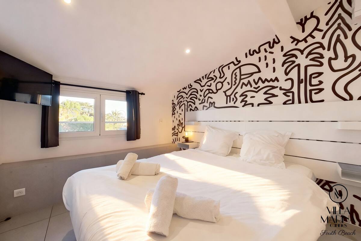 A modern bedroom with a large bed, white linens, and a decorative wall mural.