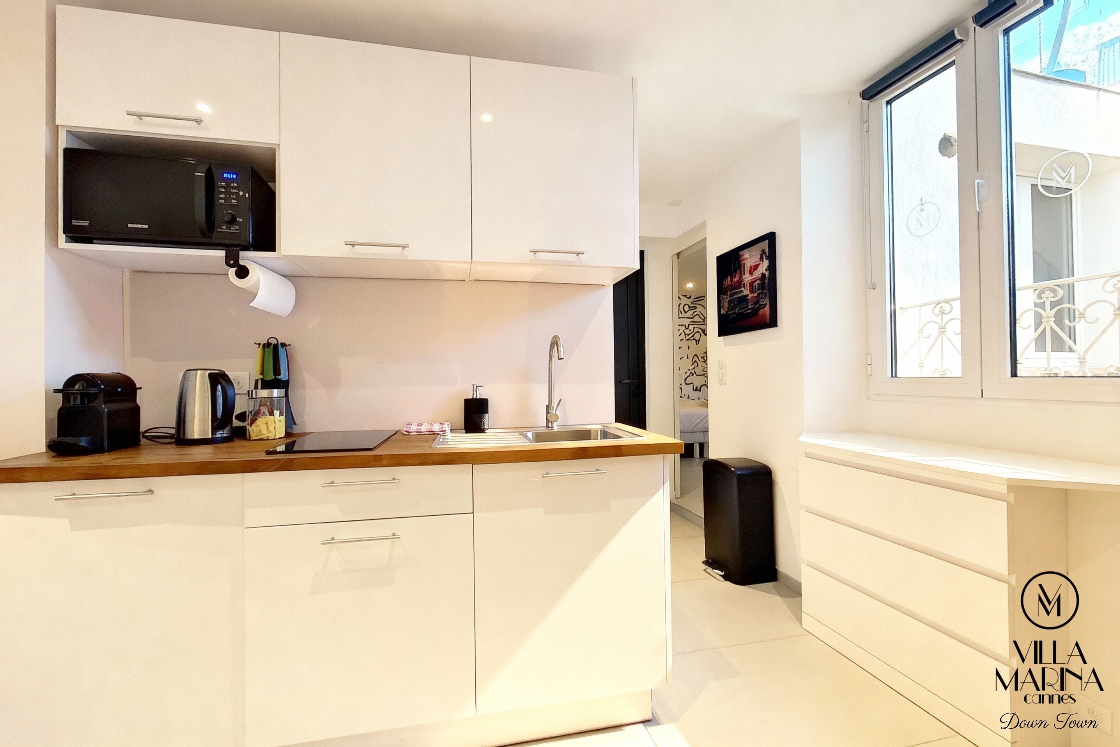 A modern kitchen with white cabinetry, a built-in microwave, a kettle, and a sink.