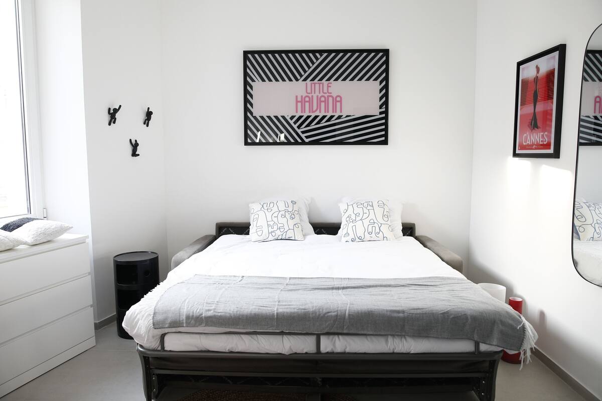 A bedroom with a bed, a bedside table, a lamp, a mirror, and wall art.