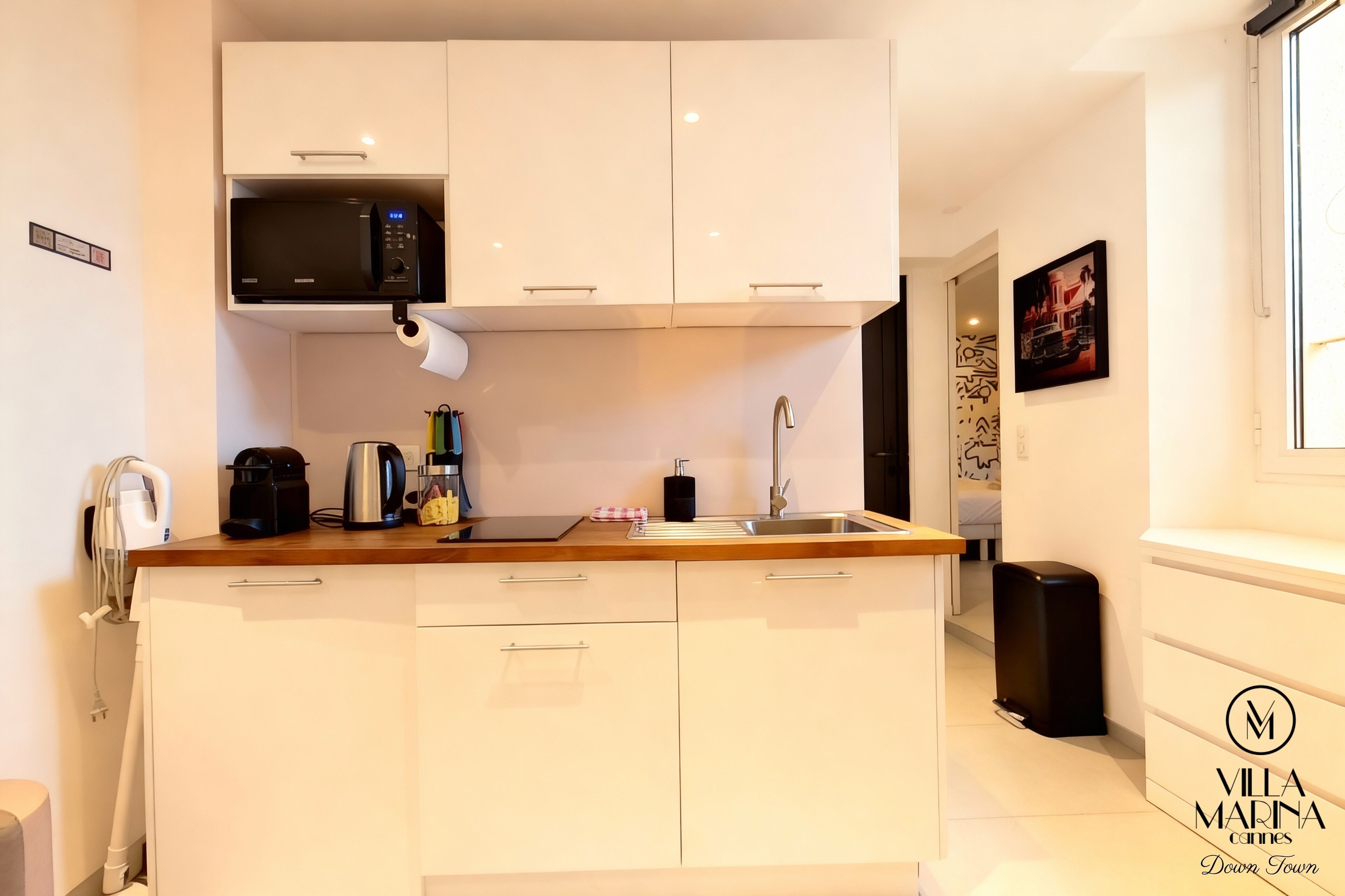 Een moderne keuken met witte kastjes, een ingebouwde magnetron, een koffiezetapparaat en een spoelbak.