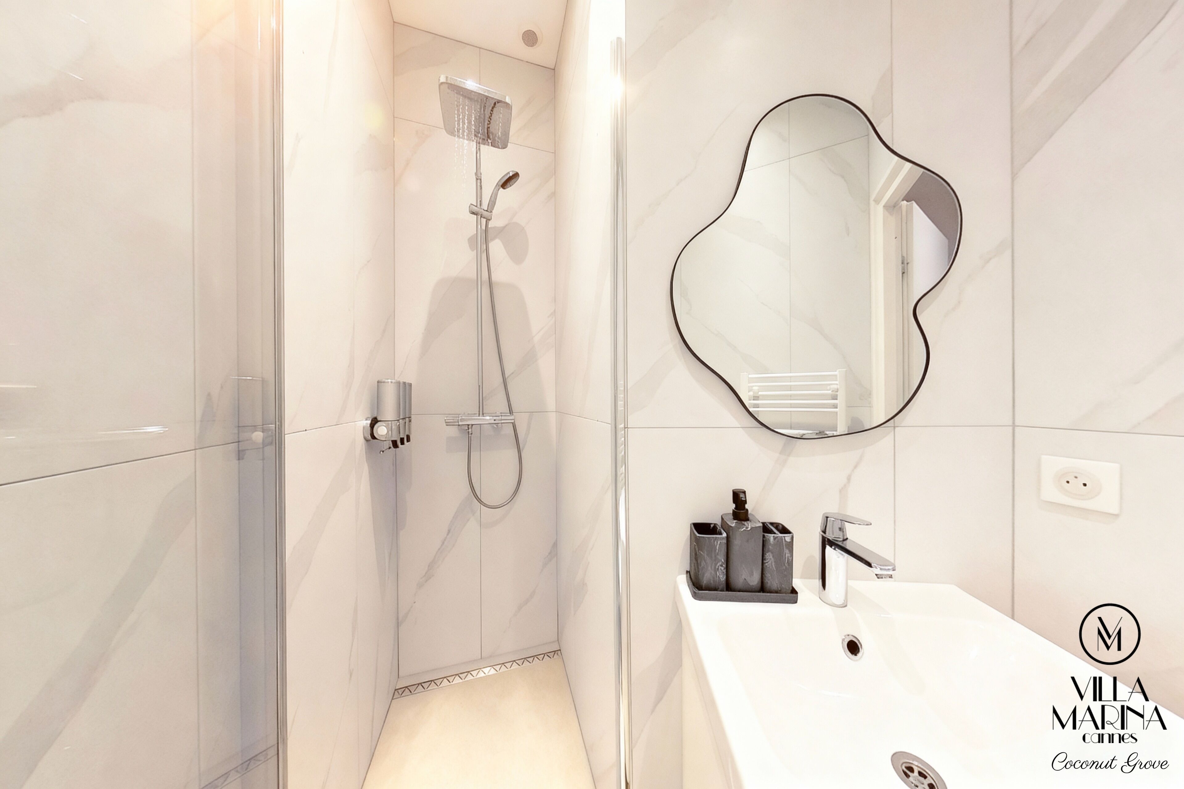 Ein modernes Badezimmer mit einer gläsernen Dusche, einem weißen Waschbecken mit Spiegel und einem Fliesenboden.