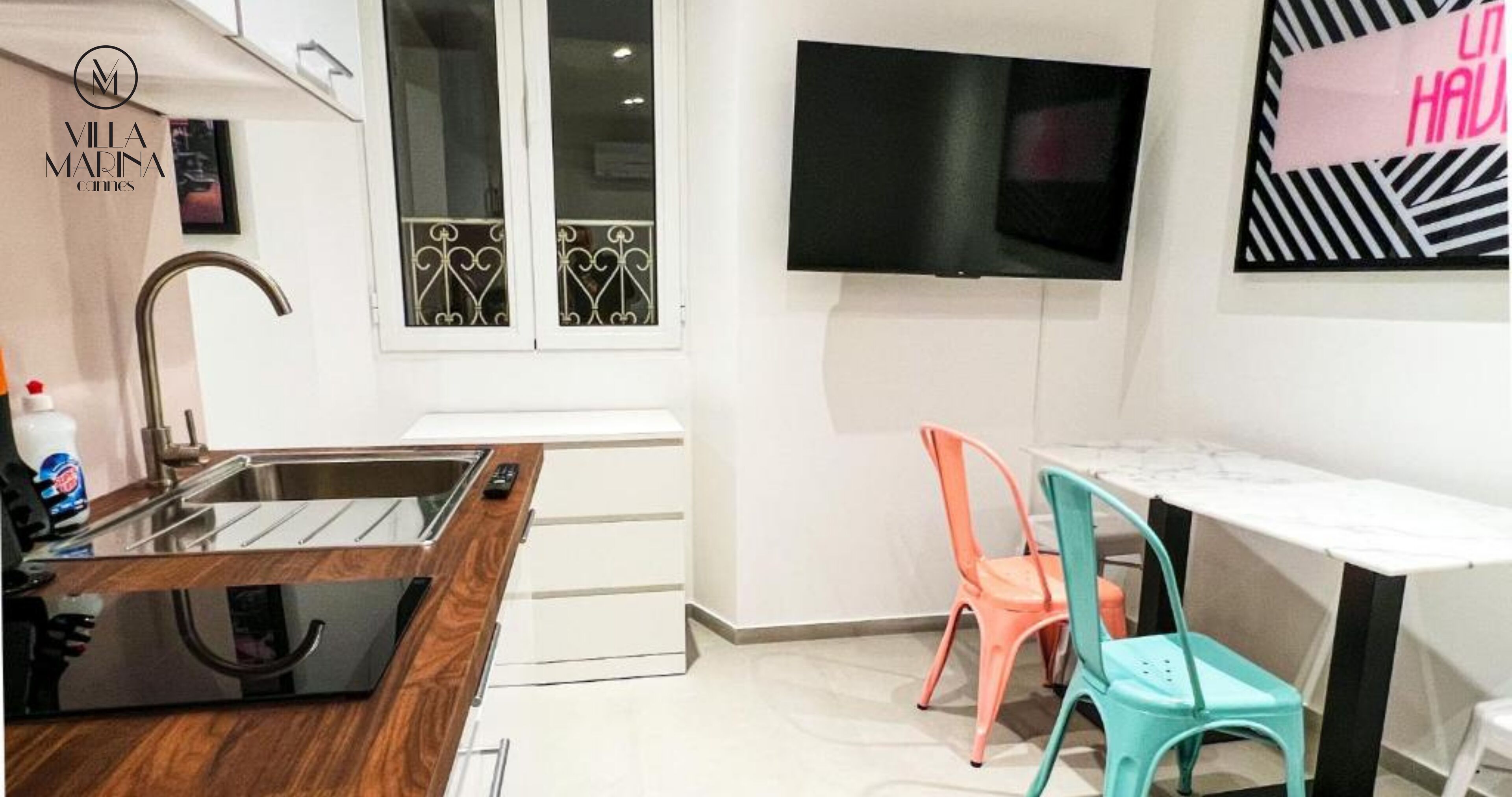 A modern kitchen with a sink, wooden countertop, and a TV mounted on the wall.