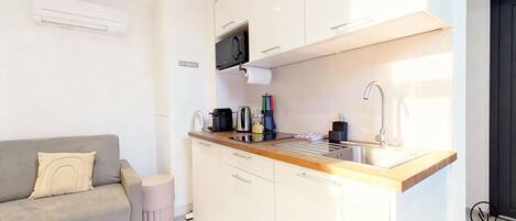 A modern kitchen with white cabinets, a grey sofa, and a small round stool.