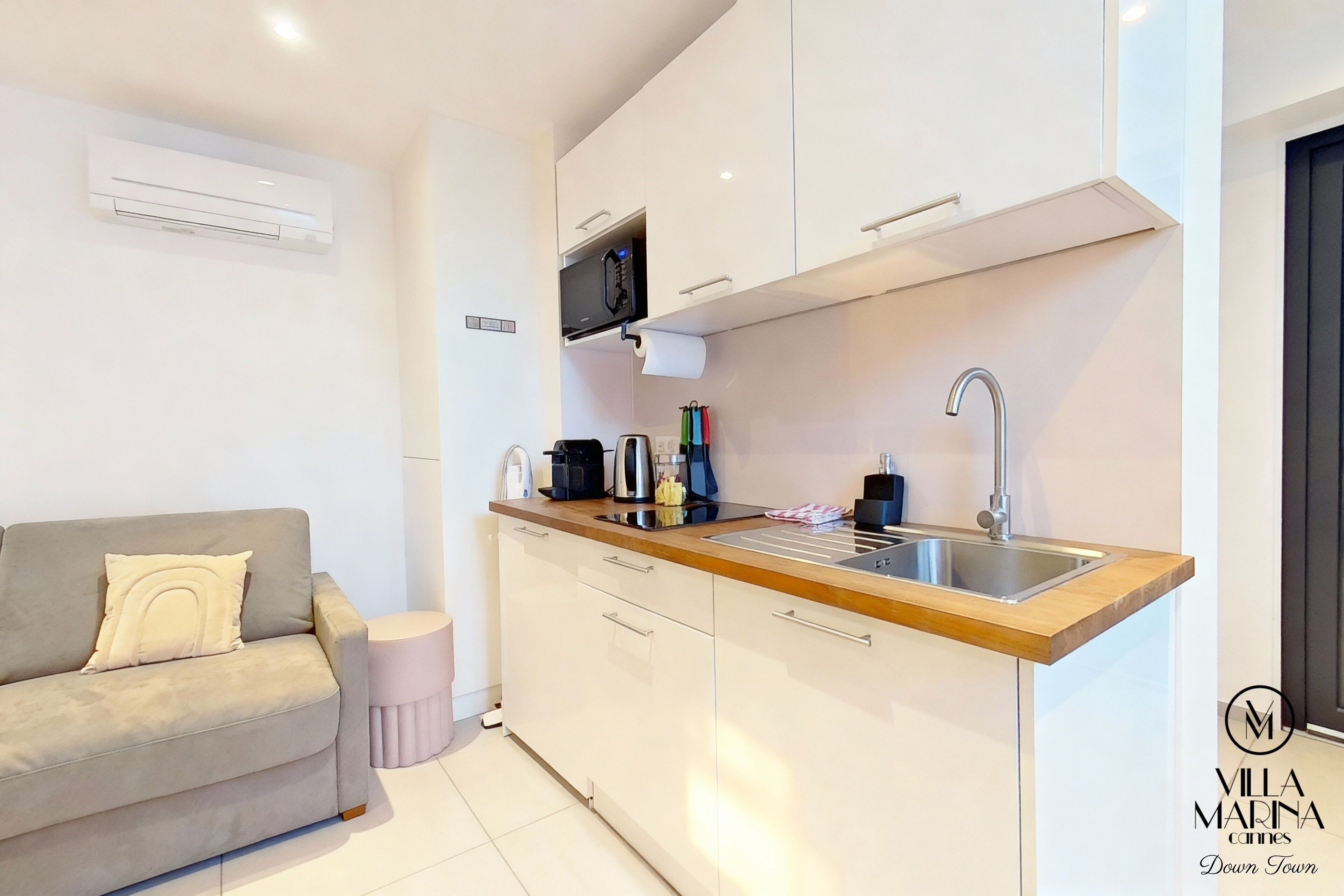 A modern kitchen with white cabinets, a wooden countertop, and a stainless steel sink.