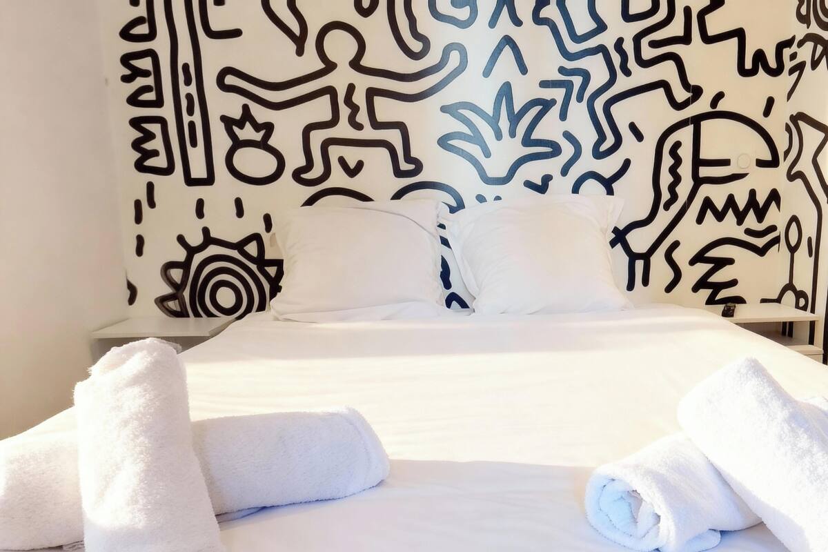 A hotel room with a bed, white linens, and a patterned wall. There are towels on the bed.