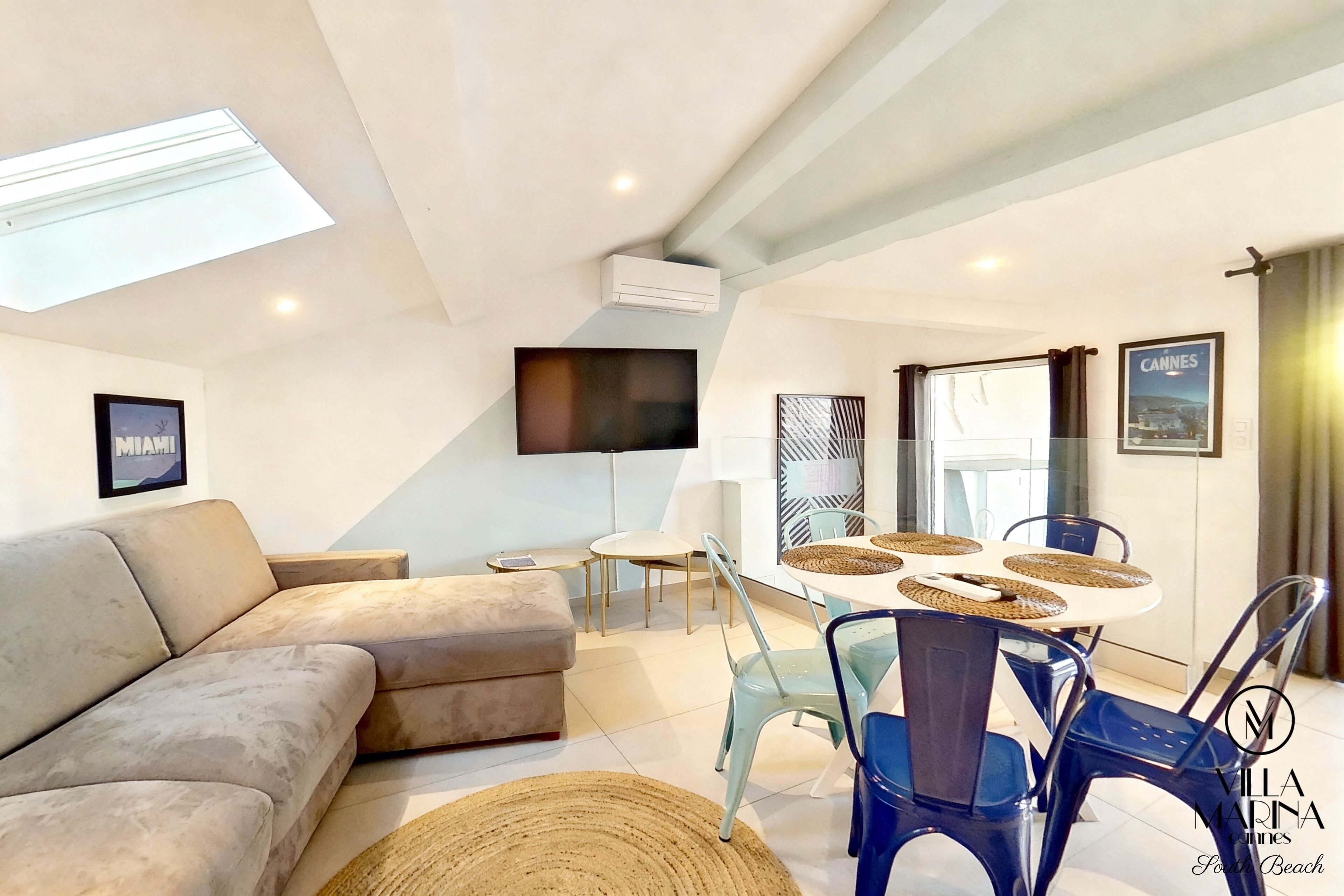 A modern living room with a sofa, a TV, a dining table with chairs, and a ceiling light.