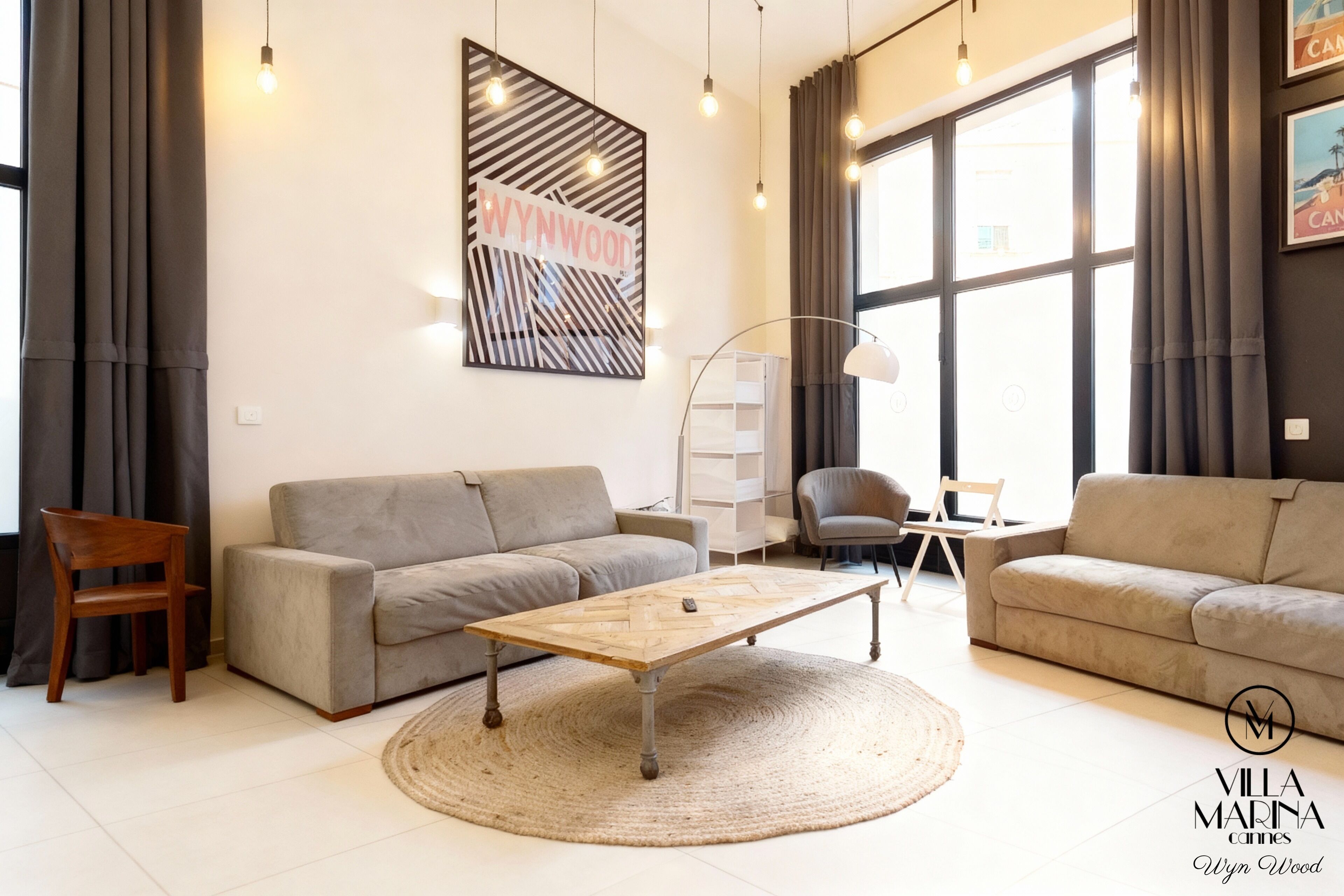 A modern living room with a wooden coffee table, two grey sofas, a wooden chair, and a large window with curtains.