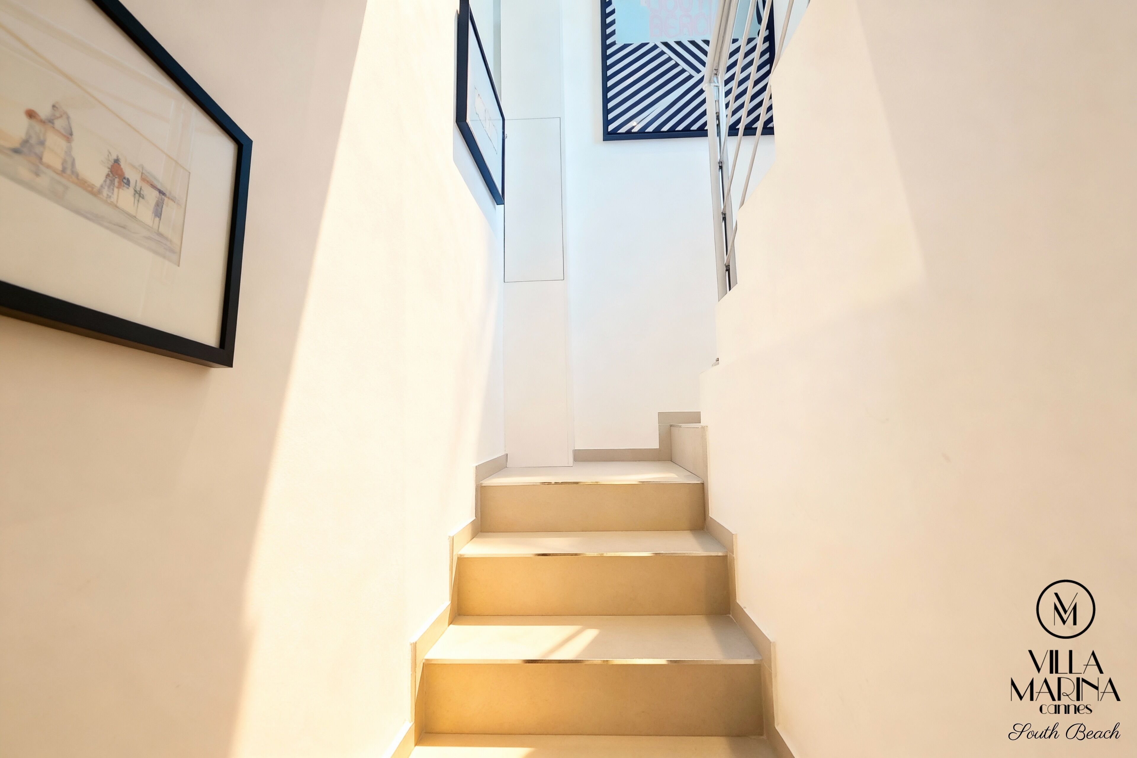 Escadaria com design minimalista, obras de arte emolduradas nas paredes e logotipo da Villa Marina Cannes South Beach.