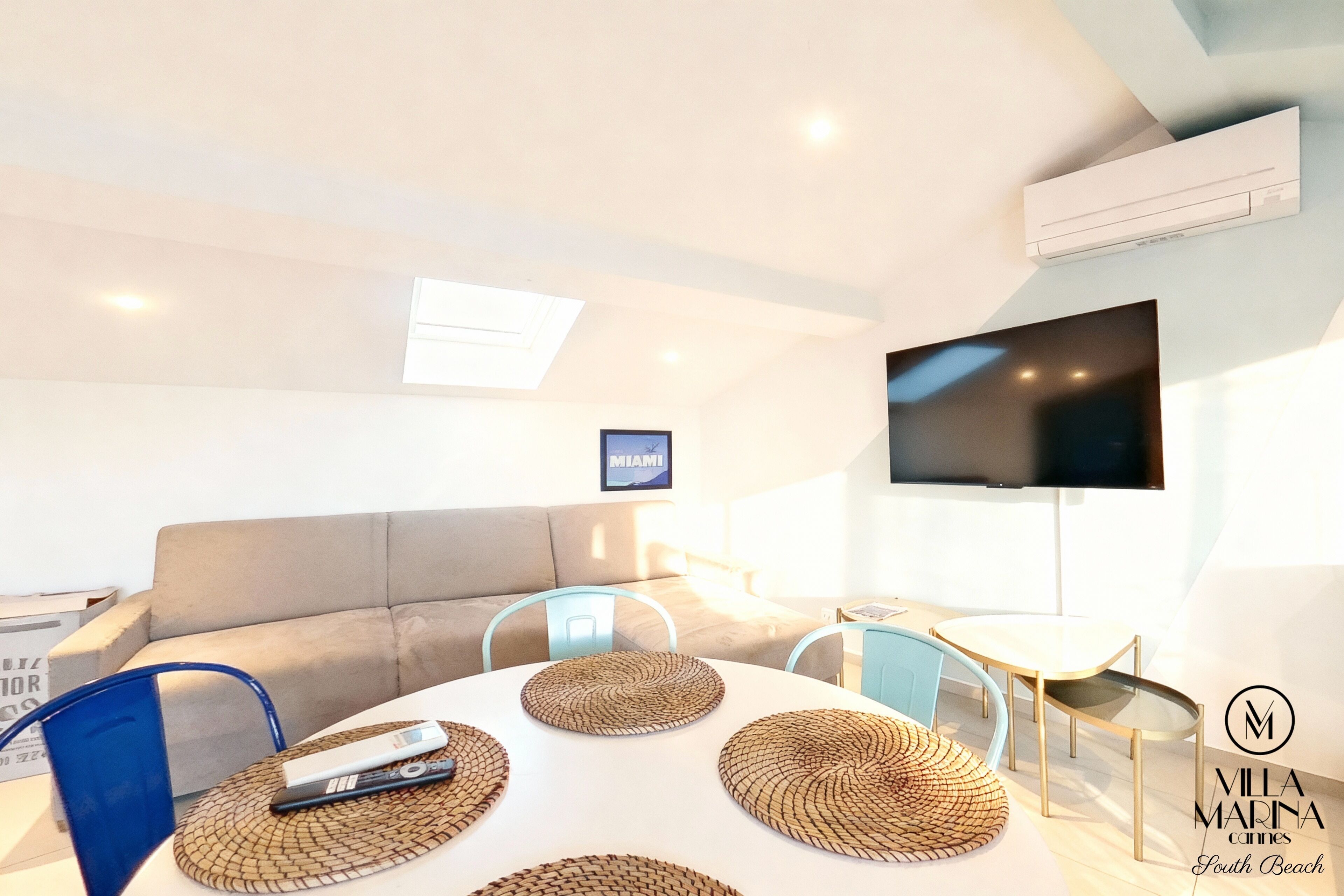 Un salon moderne avec un canapé, un téléviseur fixé au mur et un coin repas comprenant une table et des chaises.