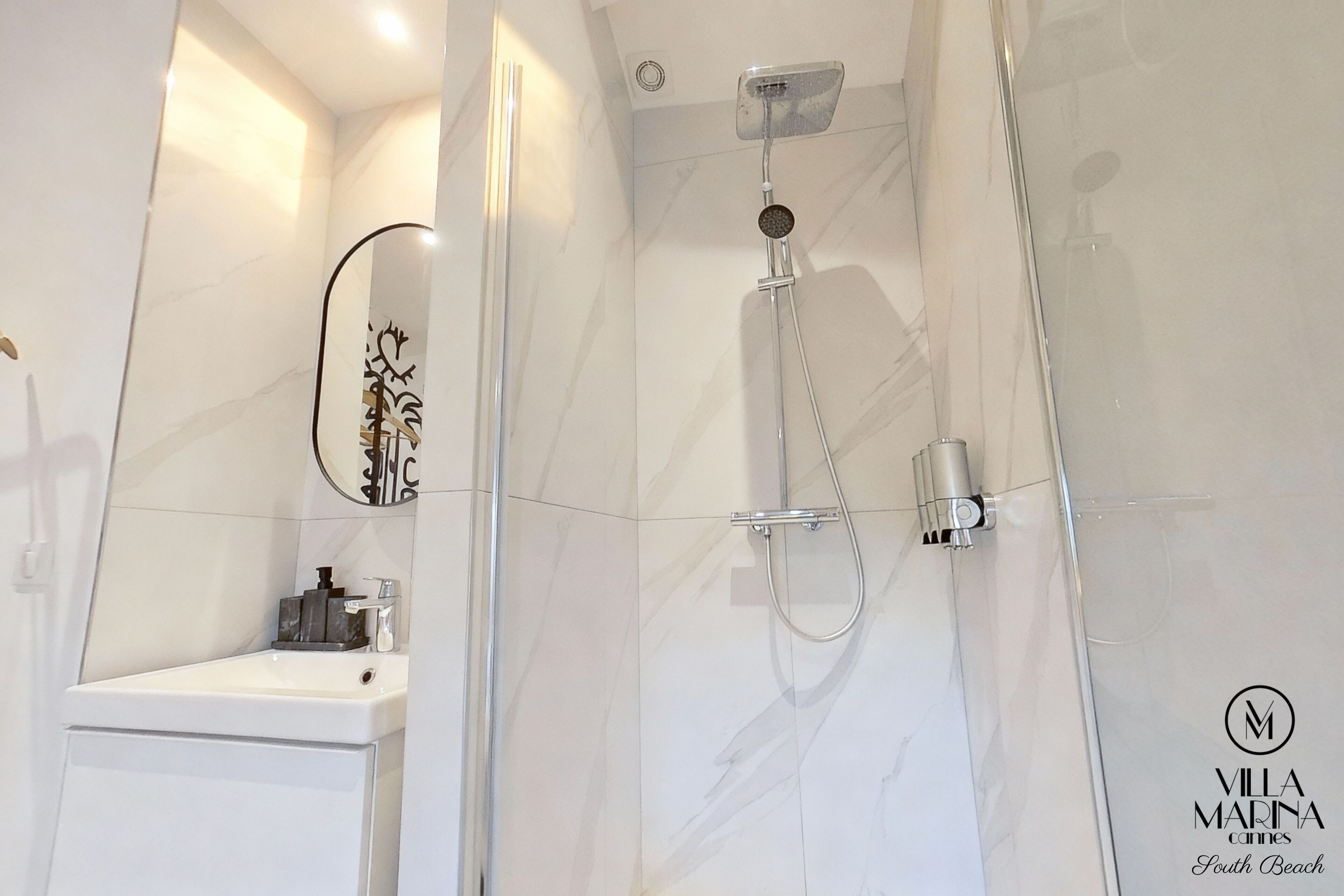 A modern bathroom with a glass-enclosed shower, a white sink, and a mirror with a decorative frame.