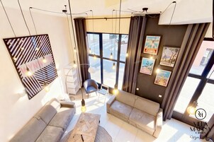 A modern living room with a sofa, a coffee table, and a chair. There are large windows with curtains, and the room has a minimalist design.