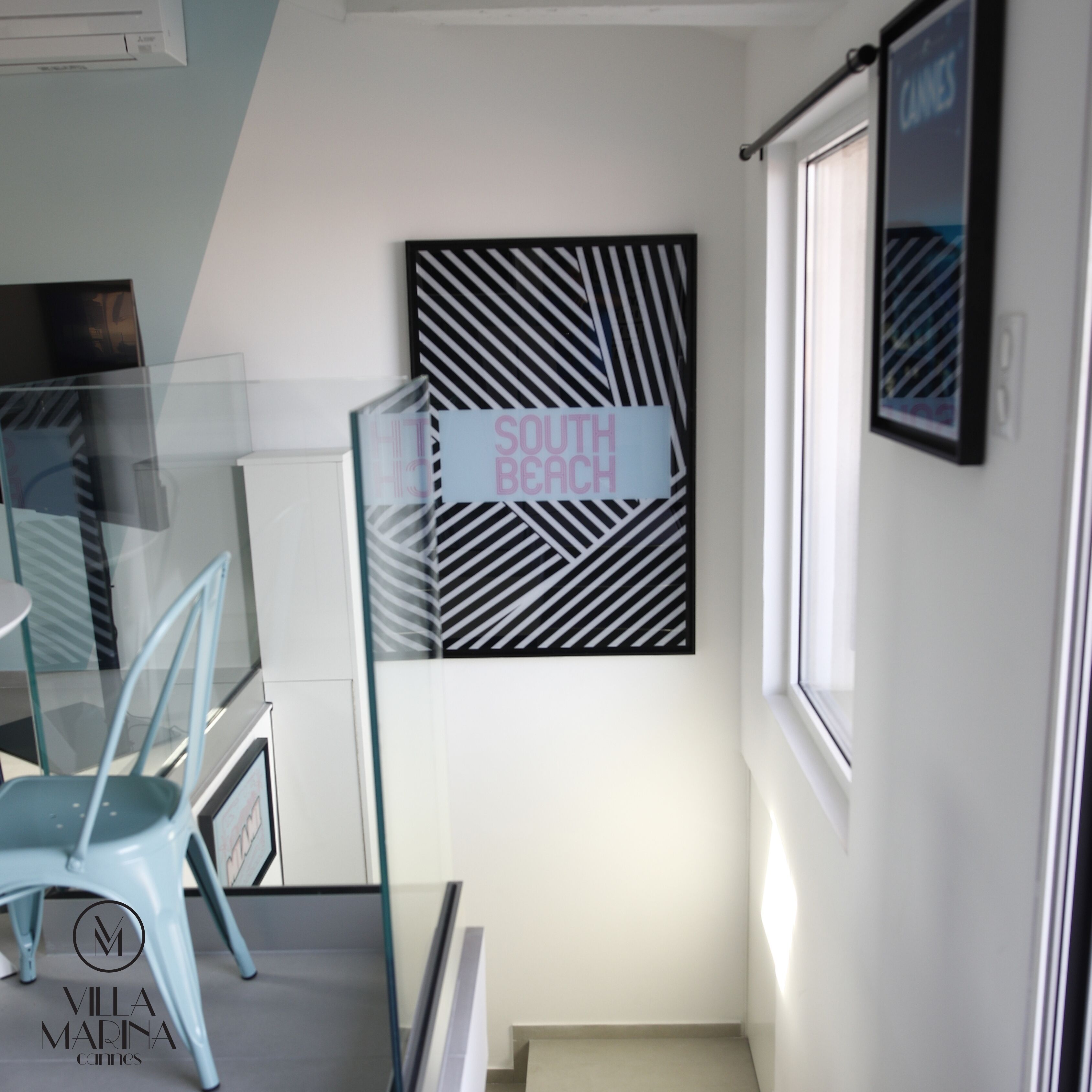 A modern interior with a glass partition, a framed artwork with 'SOUTH BEACH' text, and a 'VILLA MARINA' logo.