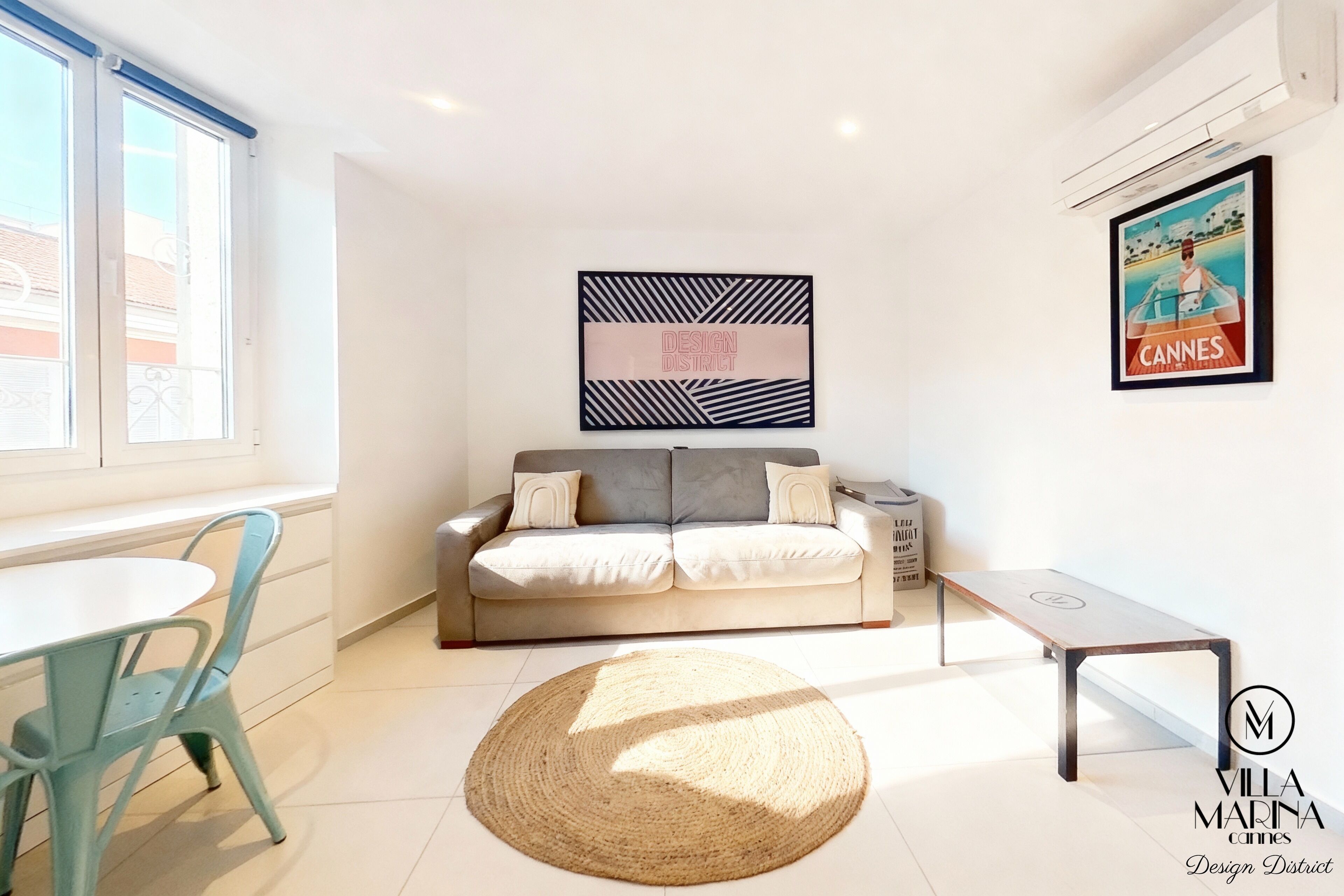 A modern living room with a sofa, a round woven rug, a small table, and a framed picture on the wall.