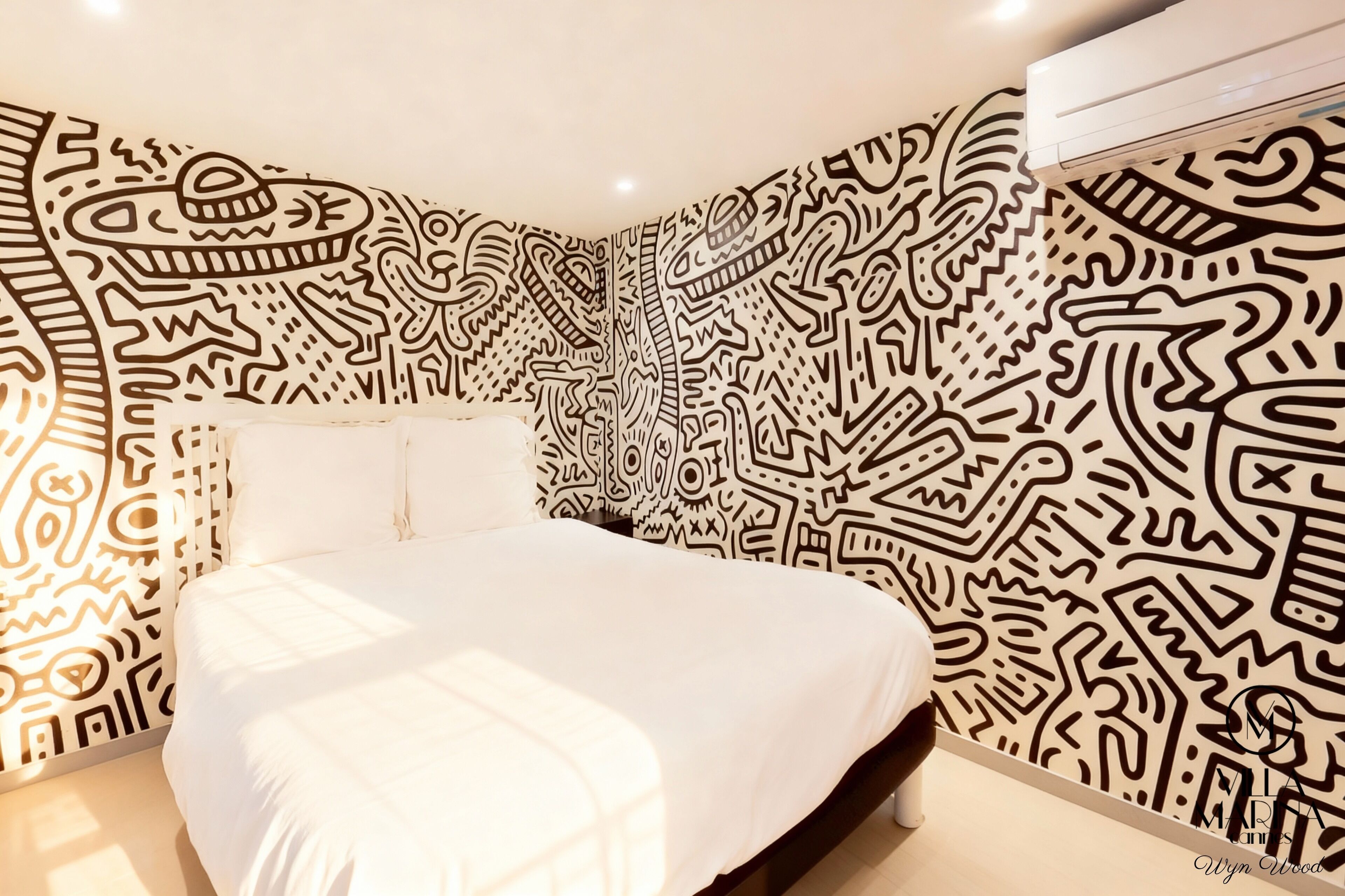 A bedroom with a bed centered in the room, surrounded by walls with intricate black patterns.