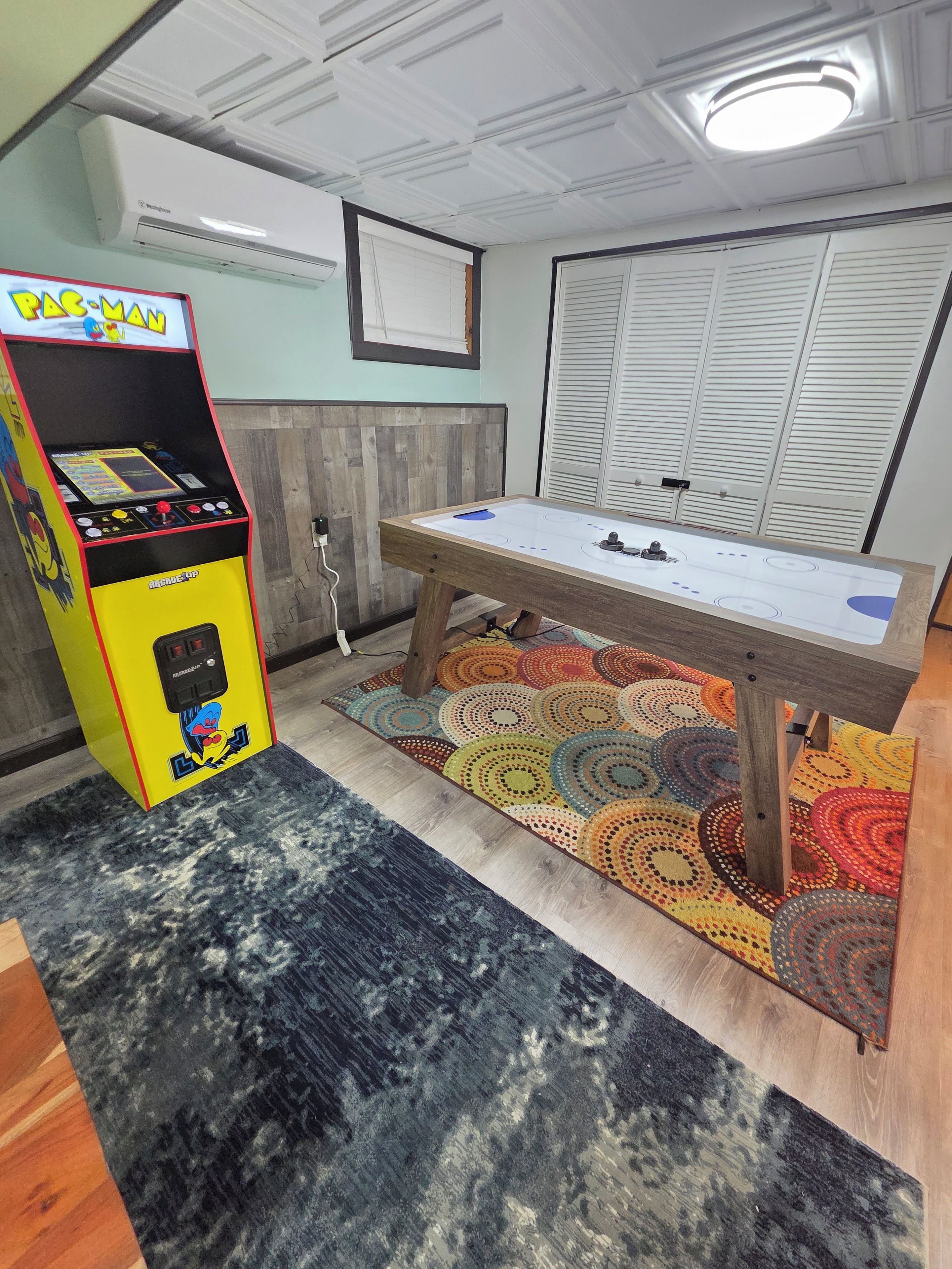 Ein Zimmer mit einem Tischkicker, einer Pac-Man-Spielmaschine und einem gemusterten Teppich.