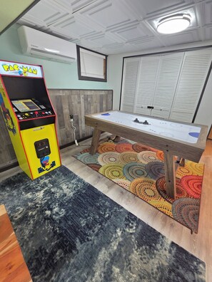 A room with a foosball table, a Pac-Man arcade machine, and a patterned rug.