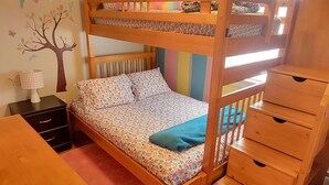 Habitación con literas, un escritorio de madera, un aparador y un vinilo decorativo en la pared.